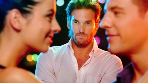 Handsome jealous man looking at flirting couple on dance floor