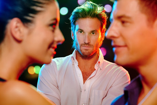 Handsome jealous man looking at flirting couple on dance floor