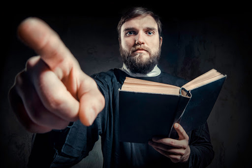 Priest with Prayer book against dark background &#8211; it