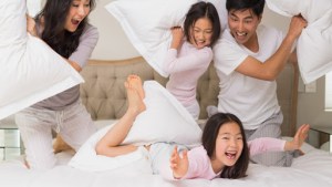 Cheerful kids and parents having pillow fight on bed at home – it