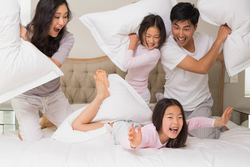Cheerful kids and parents having pillow fight on bed at home &#8211; it