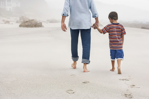 Father and son holding hands while walking on sand at beach