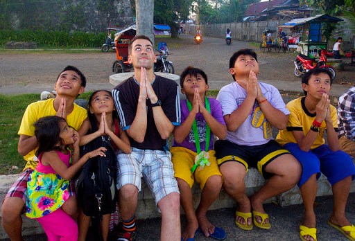 Joven misionero rezando con un grupo de niños &#8211; it