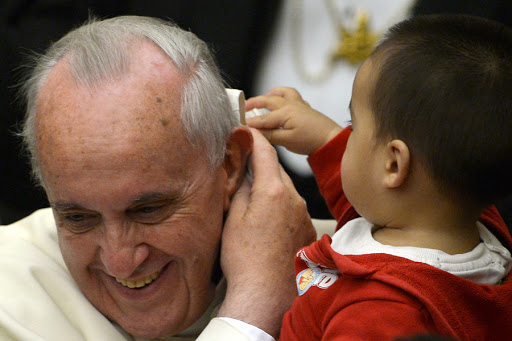 A child plays with Pope Francis&#8217; skull cap during an audience with beneficiaries and volunteers of the Santa Marta pediatric dispensary &#8211; it
