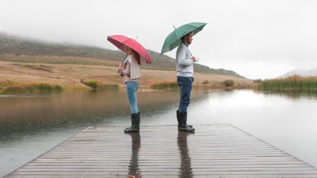 Couple standing in the rain on wooden boardwalk with umbrellas