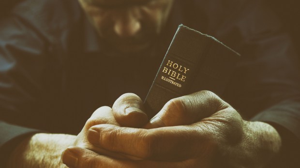 A Man praying holding a Holy Bible.