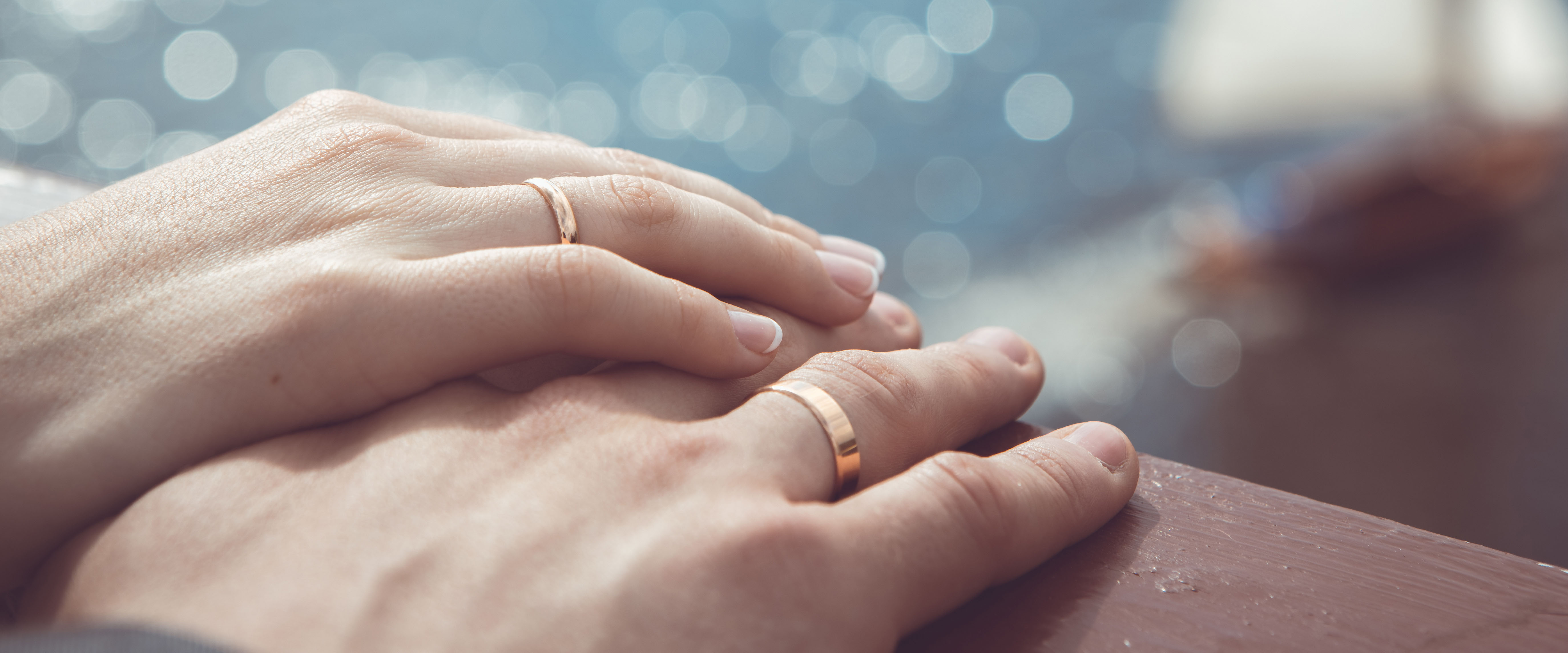 Holding Hands with wedding rings on the background of sea and sun – shutterstock_167534945 HERO