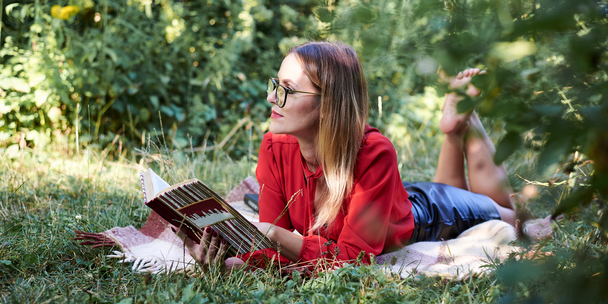 web3-young-blond-woman-wearing-eyeglasses-red-blouse-and-black-skirt-laying-on-the-green-grass-in-the-park-holding-open-book-thinking-pretty-girl-reading-book-in-summer.-student-studying.jpg