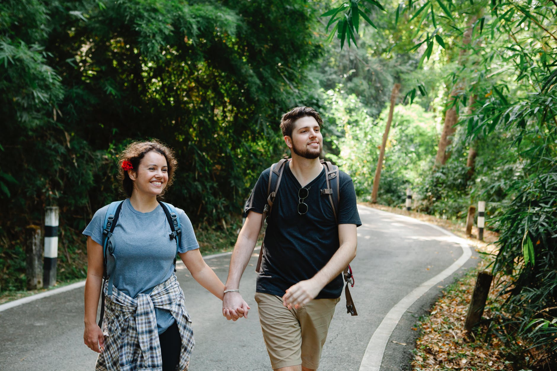 delighted couple holding hands while strolling on road in tropical park