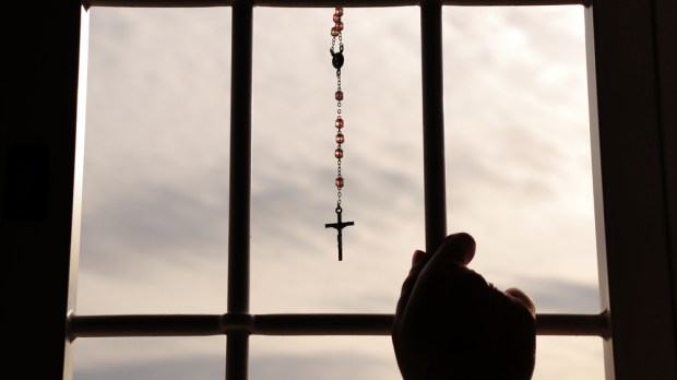 Religious rosary hanging on window with grate