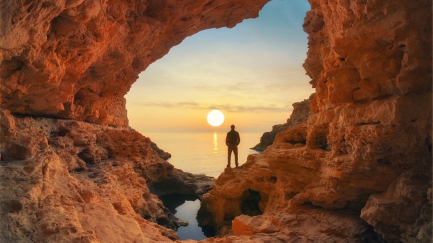 mężczyzna stoi w skalnej grocie nad brzegiem morza