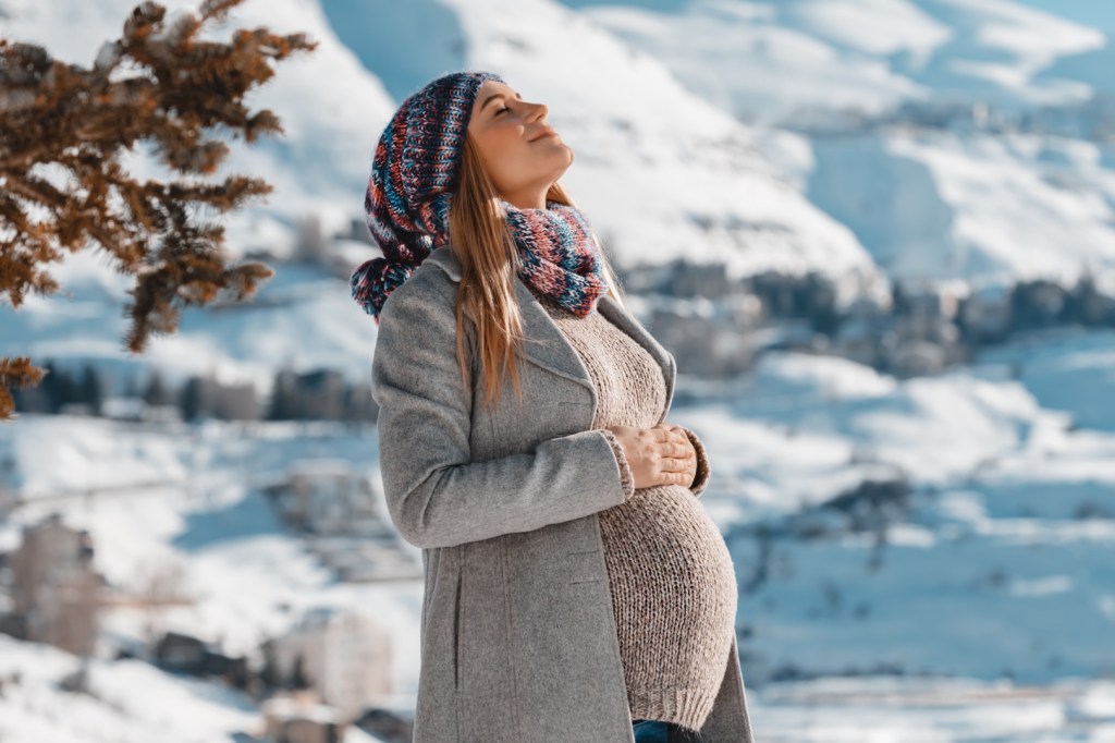 uśmiechnięta kobieta w ciąży stoi w zimie w kurorcie