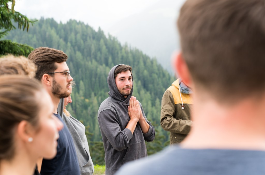 young group of men and women stand in a circle and prepare to have a group prayer outdoors