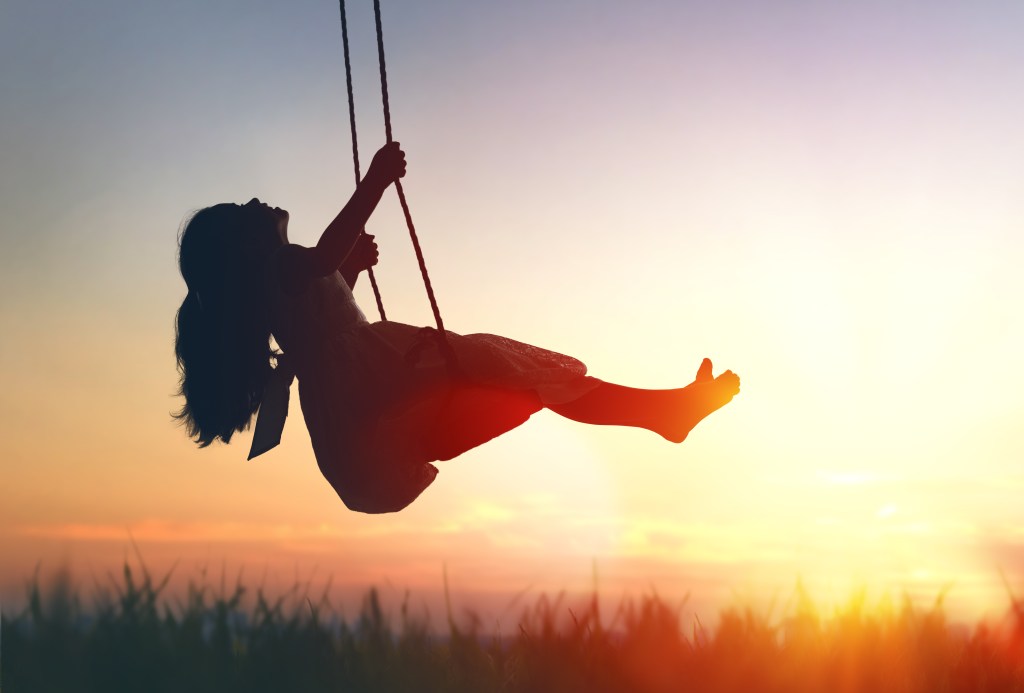 Happy laughing child girl on swing in sunset summer