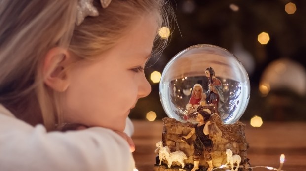 Girl looking at a glass ball with a scene of the nativity of Jesus Christ in a glass ball on a Christmas tree