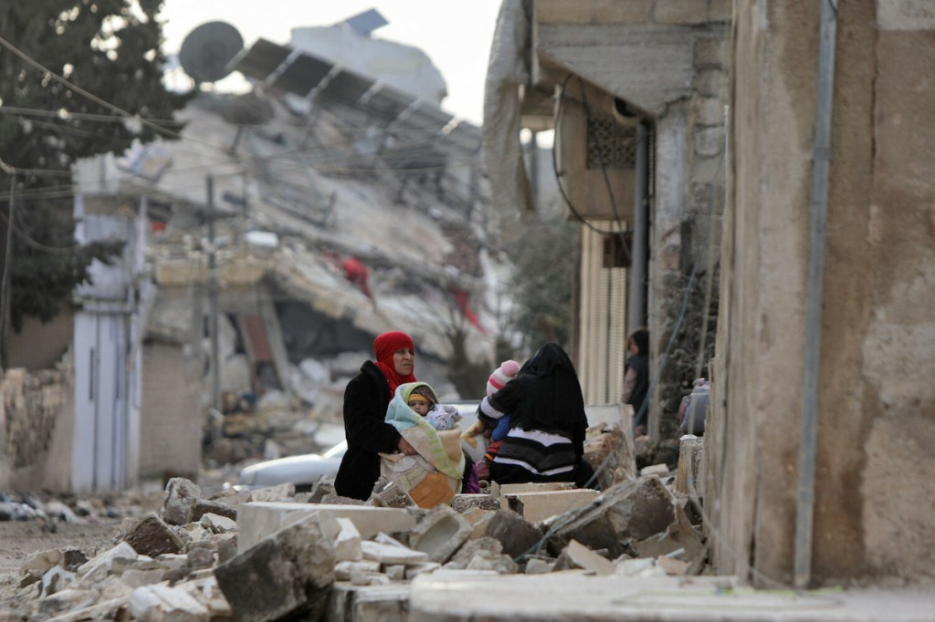 Syrian women and children sit wrapped in blankets outside collapsed buildings on February 7, 2023, in the town of Jandairis, in the rebel-held part of Aleppo province, as search and rescue operations continue following a deadly earthquake. - The death toll from the massive earthquake that struck Turkey and Syria rose above 8,300, official data showed, with rescue workers still searching for trapped survivors. (Photo by Bakr ALKASEM / AFP) - EN_01553763_1096.jpg